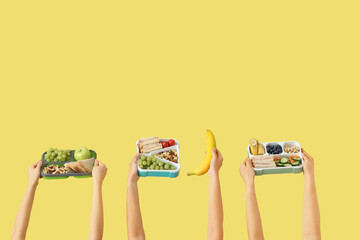 Female hands with school lunch boxes and banana on yellow background