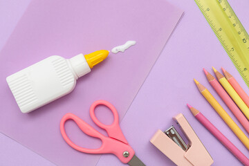 Bottle with spilled glue, sheet of paper, stapler and pencils on lilac background. Top view