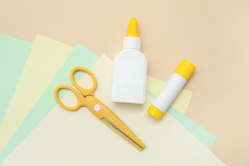 Bottle of glue, stick glue, scissors and sheets of paper on beige background. Top view