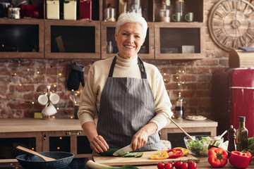 Healthy eating habits. Cheerful senior woman cutting vegetables for salad, cooking in kitchen, free space