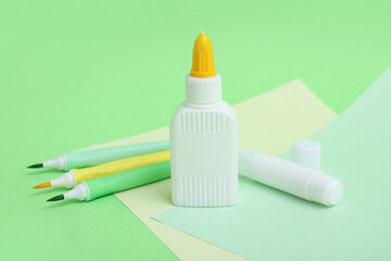 Bottles of glue, felt-tip pens and sheets of paper on green background