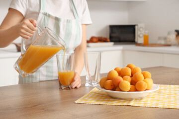 Young woman pouring apricot juice into glass in kitchen. Closeup