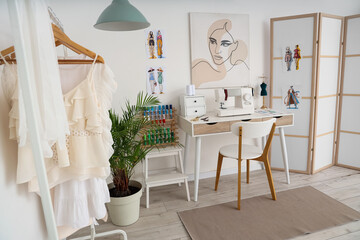 Interior of light atelier with tailor's workplace, clothes rack and folding screen