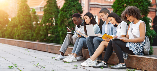 Focused students preparing for exams outdoors in the university courtyard, sitting on bench in campus
