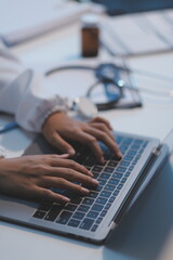 A professional and focused Asian female doctor in scrubs is working and reading medical research on her laptop in her office at a hospital.