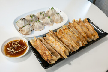 An assortment of Steamed Potstickers and Pan Fried Xiaolongbao served with dipping sauces on a white table. 