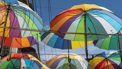 Colorful rainbow umbrellas suspended in rows above the road. Colorful parasol domes on a blue sky...