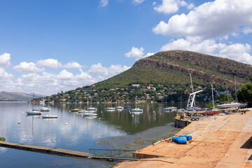 A landscape of a sloping rock layer called a cuesta against a blue and cloud sky with a reflective,...
