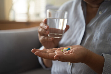 A woman hand hold glass of water and pills the palm of her hand to take painkillers, medicines, drugs,  vitamins or antibiotics capsule supplement after meal in the morning Pharmacological healthcare