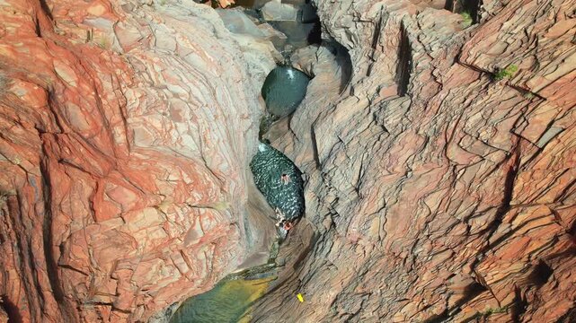 4K drone video looking down as a couple take a refreshing swim in a natural rock pool in Karijini National Park, Western Australia. This is Hamersley Gorge in the popular national park.