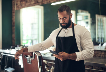 Barber, online and man with phone in salon for internet, social media and website for beauty service. Stylist, small business and hairdresser on smartphone for haircare, grooming and hairstyle