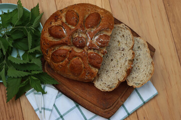 Top view of Baked homemade round bread cut in slices with nettles on wooden table with fresh nettle plants