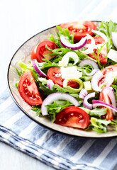 Salad with fresh tomatoes and arugula on a bright stone background. Close up. Copy space.	