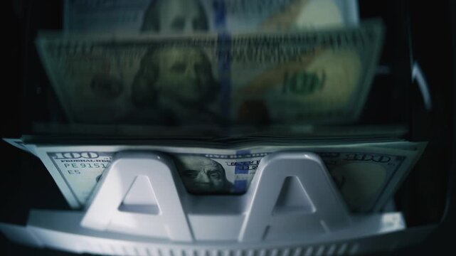 Close up of cash counting machine counting hundred dollar bills for payment or currency exchange. Automatic paper money counting equipment. 100 USD banknotes. Finance, business and banking concept.