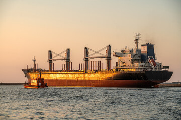 Fototapeta premium Bulk cargo vessel guided by a tugboat in the fairway to the port
