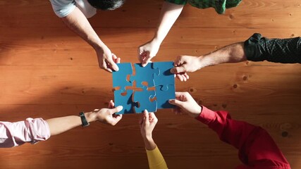 Top down view of skilled business people assemble blue jigsaw puzzle on meeting table. Group of diverse team working together to solve the puzzle. Represented togetherness, cooperative. Convocation.