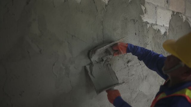 Close-up of plastering worker's hands wearing orange rubber gloves.