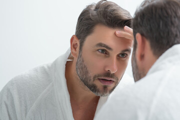 Obraz premium Close-up portrait of perfect brunet man touching chin and skin. Handsome man touching face in front of the mirror in bath. Perfect skin. Man cosmetic, skin treatment. Hygiene and skin care male face.