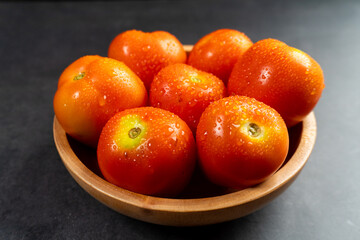 a wooden bowl of fresh red tomatoes on dark table