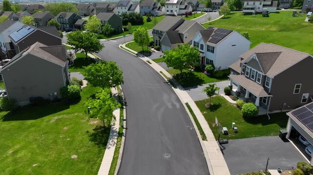 Suburban neighborhood with solar panel houses and curving streets in Pennsylvania. Residential area with green lawns and tree-lined sidewalks. Peaceful community environment aerial.