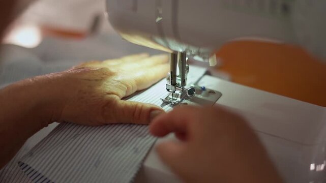 Close-up of hands guiding fabric through a sewing machine, focused on stitching