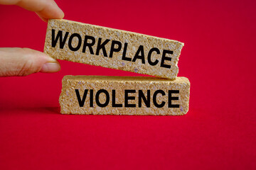 Text WORKPLACE VIOLENCE written on brick blocks on beautiful red background. businessman hand....