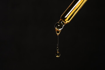 Macro photo of pipette with dripping golden liquid on black background, care product.