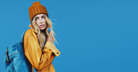 Stylish student woman in bright fall winter look and backpack on blue copy space background.