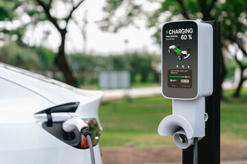 EV electric vehicle recharging battery from EV charging station in outdoor green city park scenic....