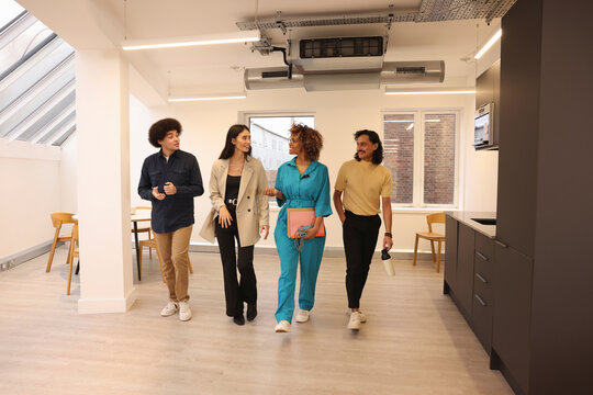 Four smiling colleagues walking through kitchen section in modern creative studio