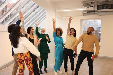 Multiethnic group of smiling creative workers raising hands and cheering in modern office