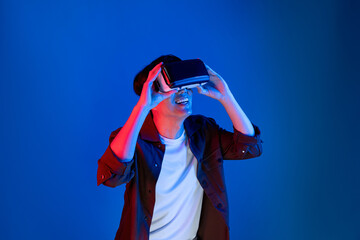 Asian man looking through VR enjoy watching fantastic meta on interesting object technology blue neon lighting background on virtual reality metaverse new world in 3D hologram innovation. Contrivance.