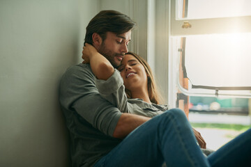 Couple, happy and relax by window in house for comfort, love and bonding time together with trust and care. Man, woman and hug or cuddle in home for connection, relationship and support on weekend