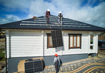 Men mounters installing solar panel system on roof of house. Workers in helmets lifting up...