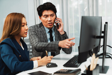 Fototapeta premium Businessman calling with business partner on mobile phone while calculating stock exchange value database with woman coworker on computer, analyzing company value sell or buy on up to date. Infobahn.