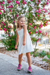 Little girl in white dress happy smiling on blooming park background in Croatia