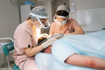 Two female doctors collecting hair follicles from donor area of male patient for hair...