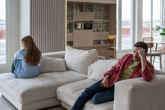Distressed and angry couple sits on opposite ends of couch after fight, ignoring each other amidst manipulative and abusive family dynamics. Toxic silence and manipulation in couple relationship
