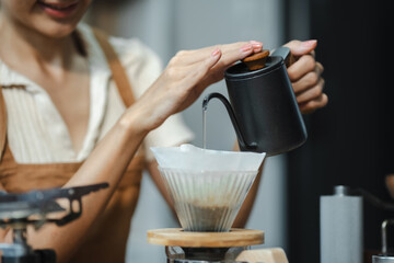 Drip coffee, woman making drip coffee by pouring spills hot water on coffee ground with prepare filter from copper pot to glass transparent chrome drip maker on wooden table.