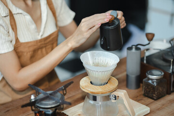 Drip coffee, woman making drip coffee by pouring spills hot water on coffee ground with prepare filter from copper pot to glass transparent chrome drip maker on wooden table.