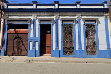 Naklejka premium One-storey Eclectic house of white facade with blue moldings, intricate grille windows, roll-up garage door, on Calle Corona Street. Santiago-Cuba-531