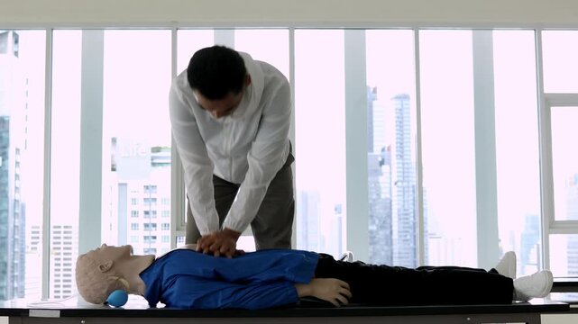 Asian man demonstrates CPR on a mannequin in a classroom setting, showcasing essential emergency response techniques for medical training purposes.