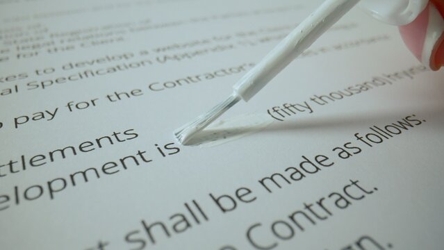 Close up shot of woman hand working with text document, liquid brush corrector in female hand draws over text, fixing the mistake.