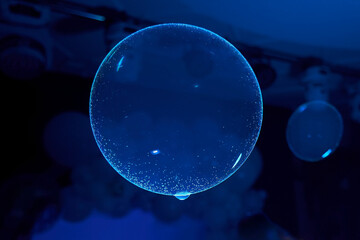 A blue bubble is floating in the air. The bubble is illuminated and he is glowing. The scene is set in a dark room