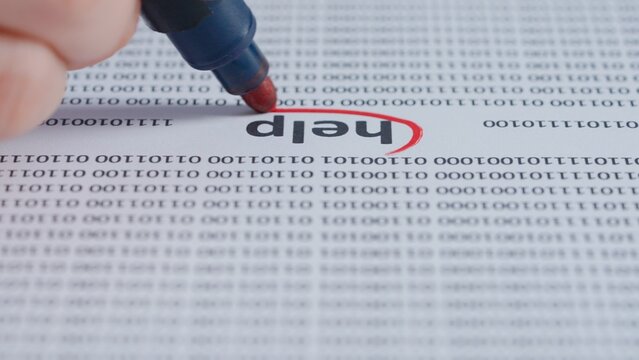 Close up shot of woman hand working with document full of binary codes, red marker in female hand marked circled a word help in text.