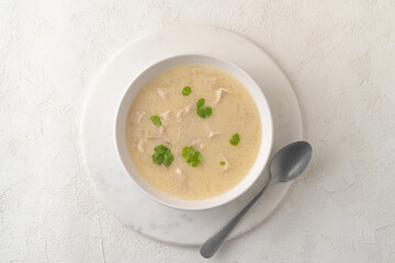 Georgian traditional chicken soup Chikhirtma in the white plate, flat lay on the light beige background