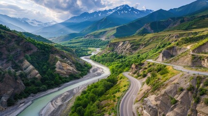 Fototapeta premium Aerial shot of Svanetia's beautiful road along a river, framed by Alpine peaks and summer greenery