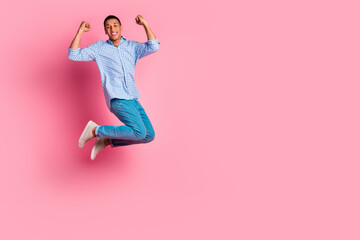 Full length photo of lucky funny guy wear plaid shirt jumping high rising fists emtpy space isolated pink color background