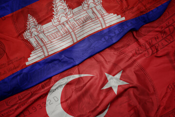 waving colorful flag of cambodia and national flag of turkey on the dollar money background....