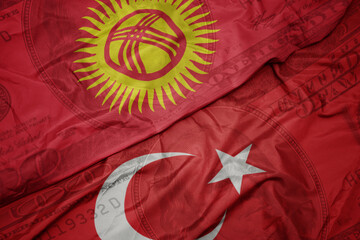waving colorful flag of kyrgyzstan and national flag of turkey on the dollar money background....
